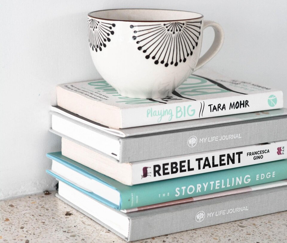 A stack of books with a white coffee cup on top