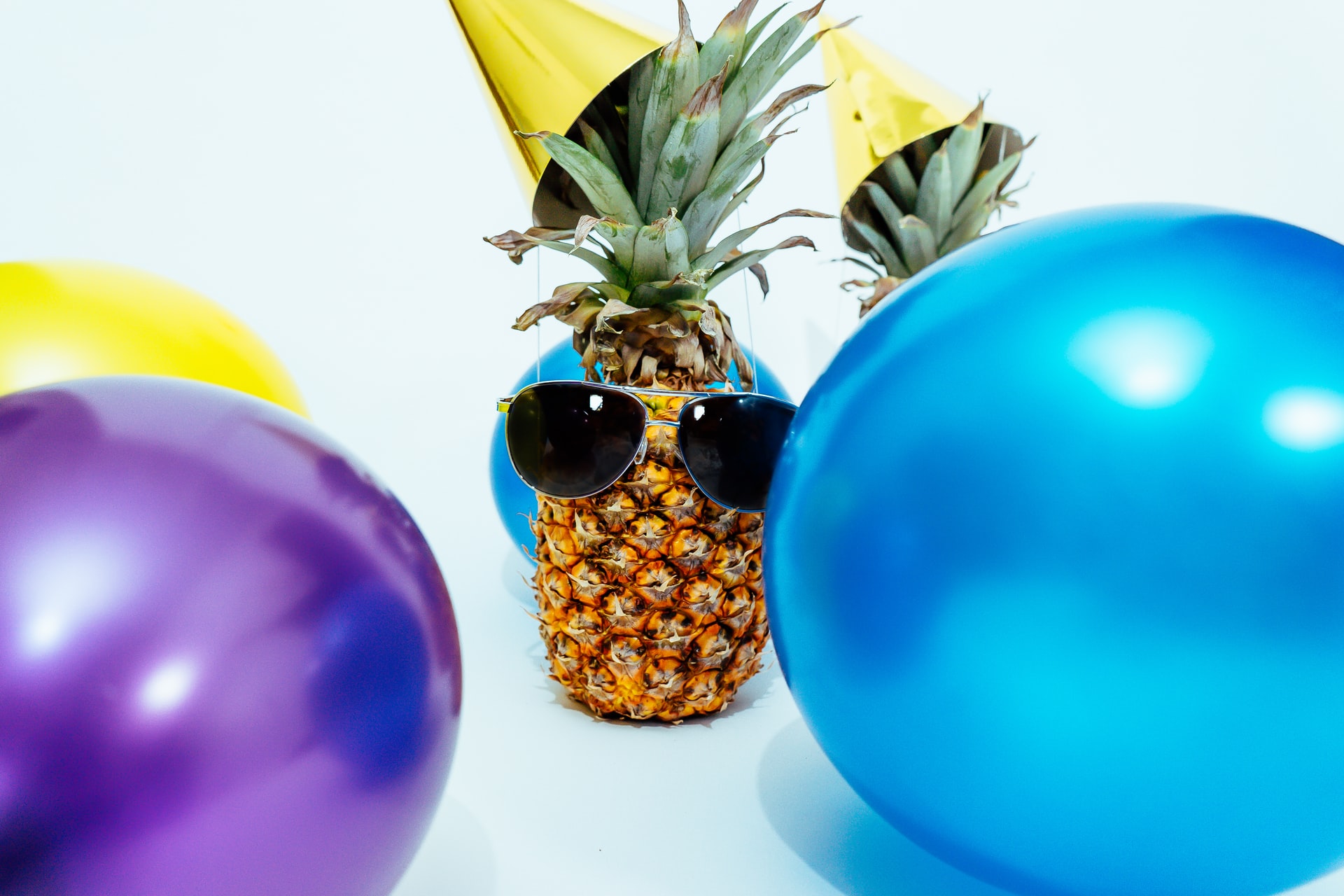 A pineapple wearing black glasses and surrounded by balloons to symbolize parties