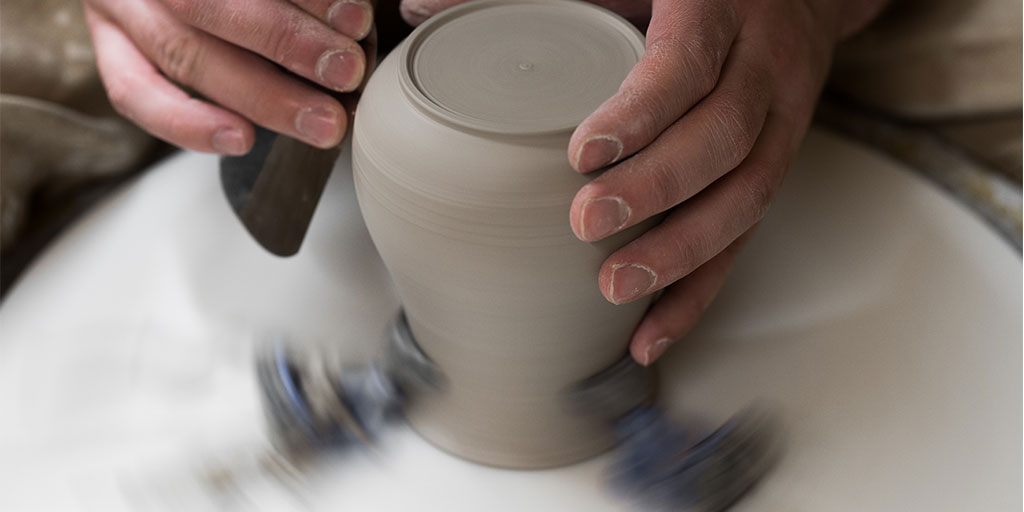 close up photo of a person's hands, modelling a clay pot on the wheel