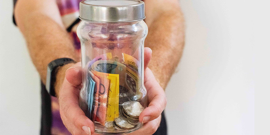A person holding a jar of coins and notes