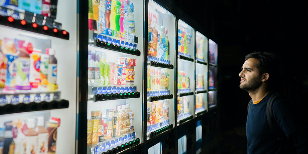 An Asian man looking at a vending machine, trying to choose a product to purchase