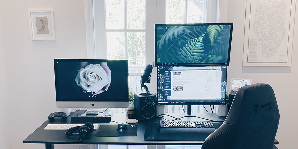 a desk with three computer screens and a microphone, two of the computer screens have a wallpaper on them and the third one has a product screen open on it
