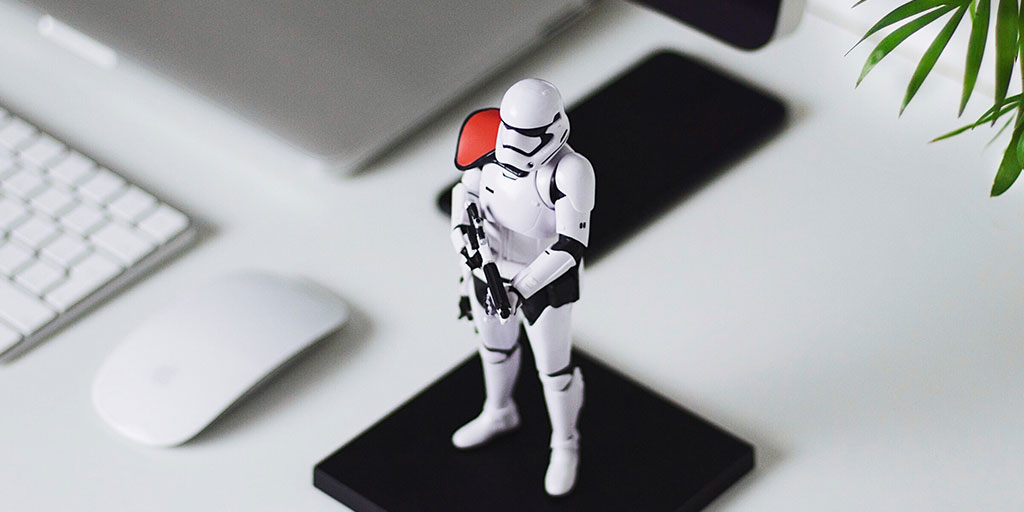an image of a toy Stormtrooper (from the Star Wars franchise) standing on a desk guarding a computer