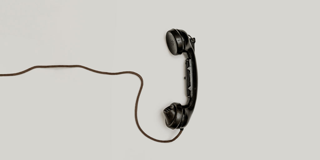 a black telephone receiver with its cord extending to the end of the picture
