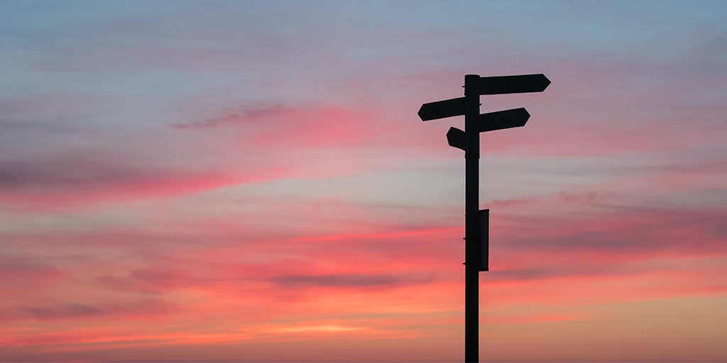 silhouette of a street sign pointing in different directions with the sun setting in the horizon